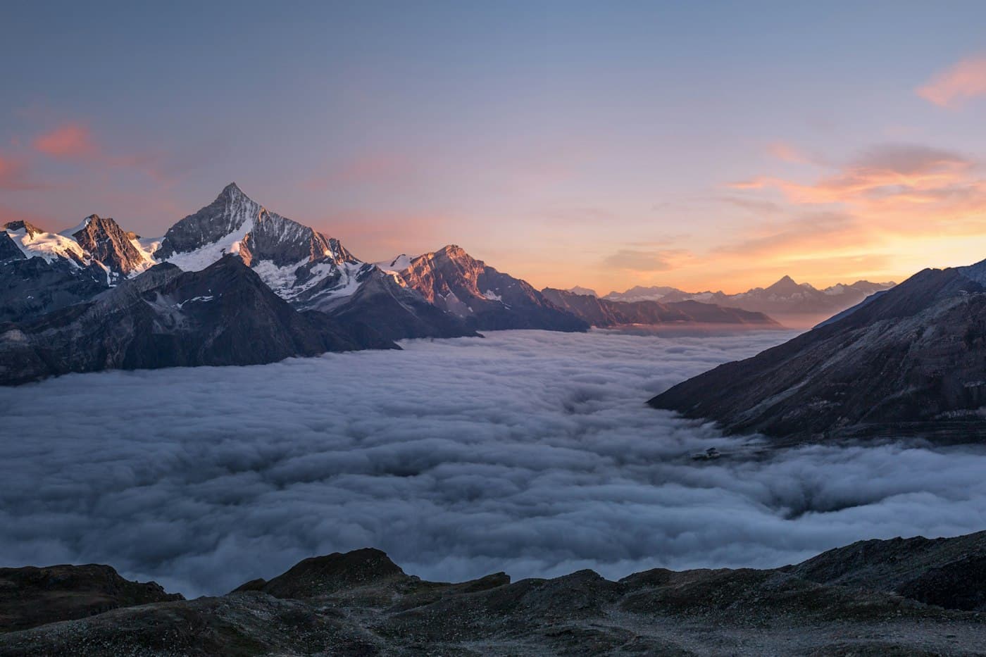 Snow-capped mountain peaks rising above a sea of clouds at dawn.